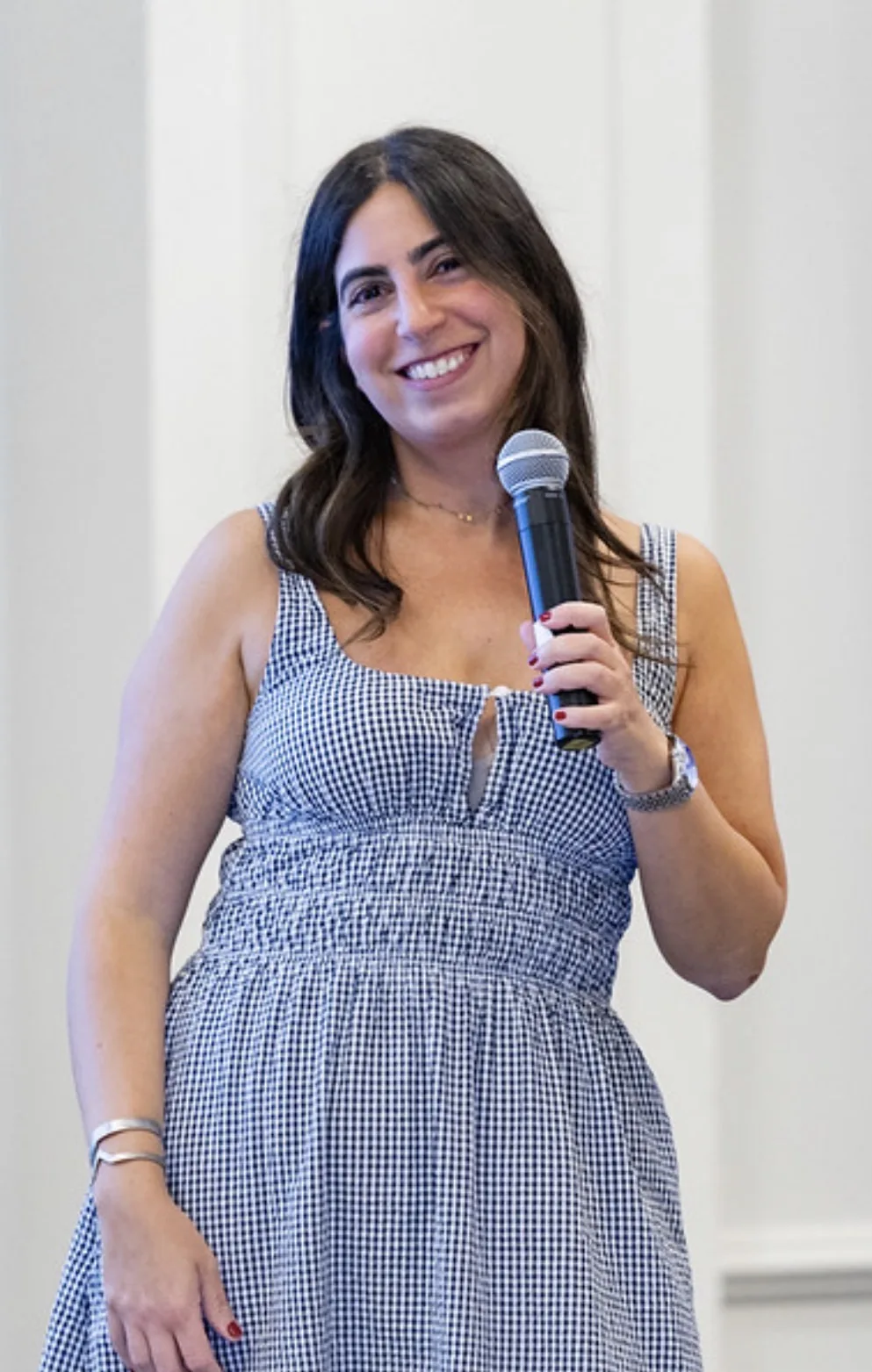 Sheena smiling in a gingham dress, holding a microphone